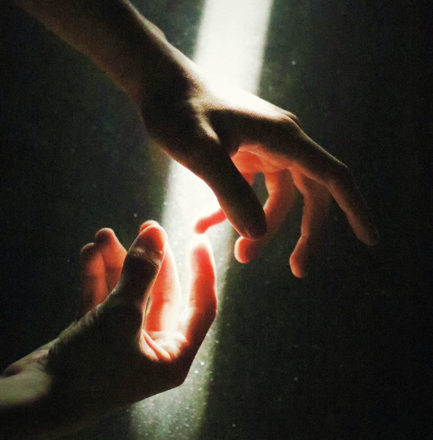 Two hands reaching for each other illuminated by a shaft of light.