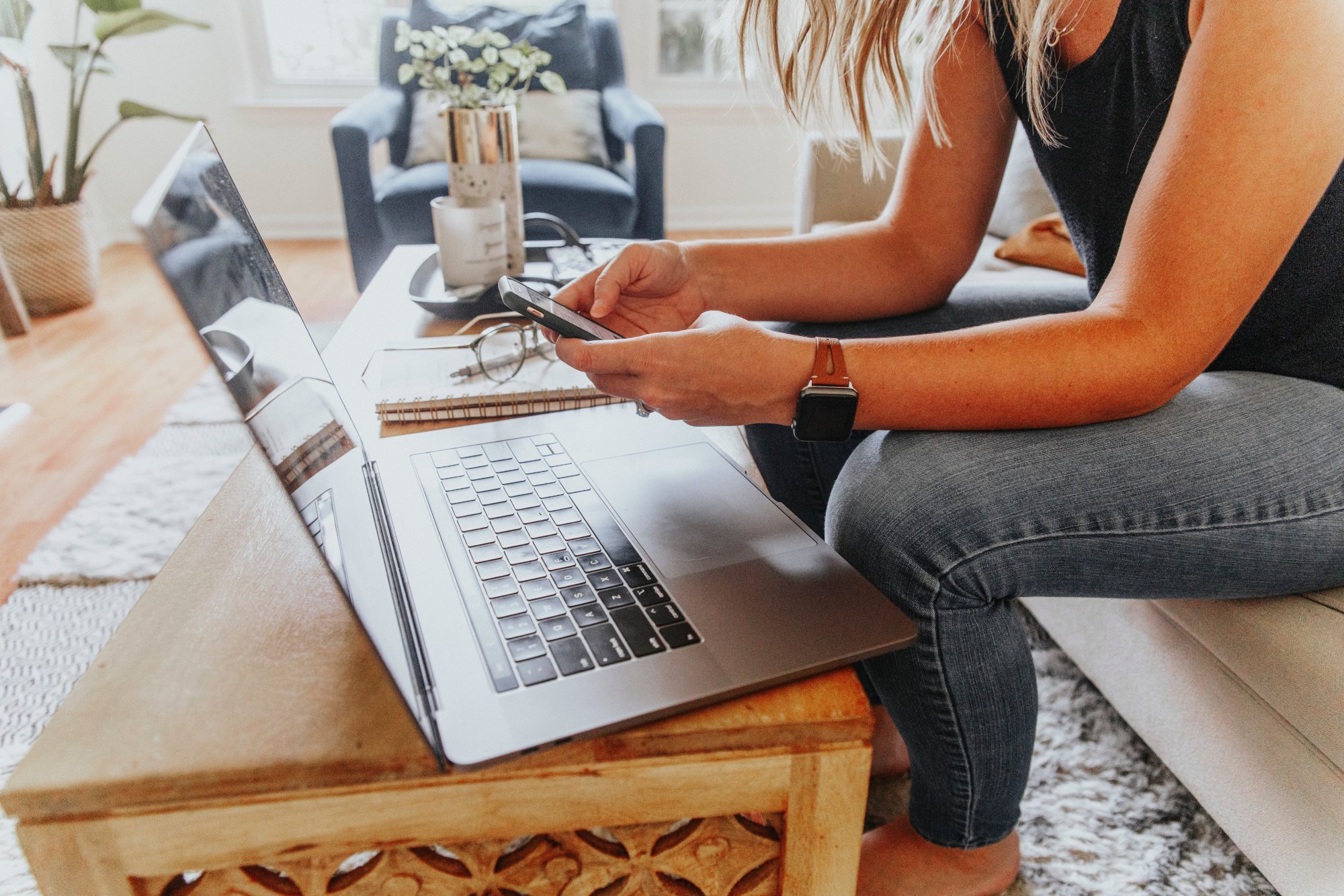 A woman in front of a laptop holding a mobile phone multitasking.