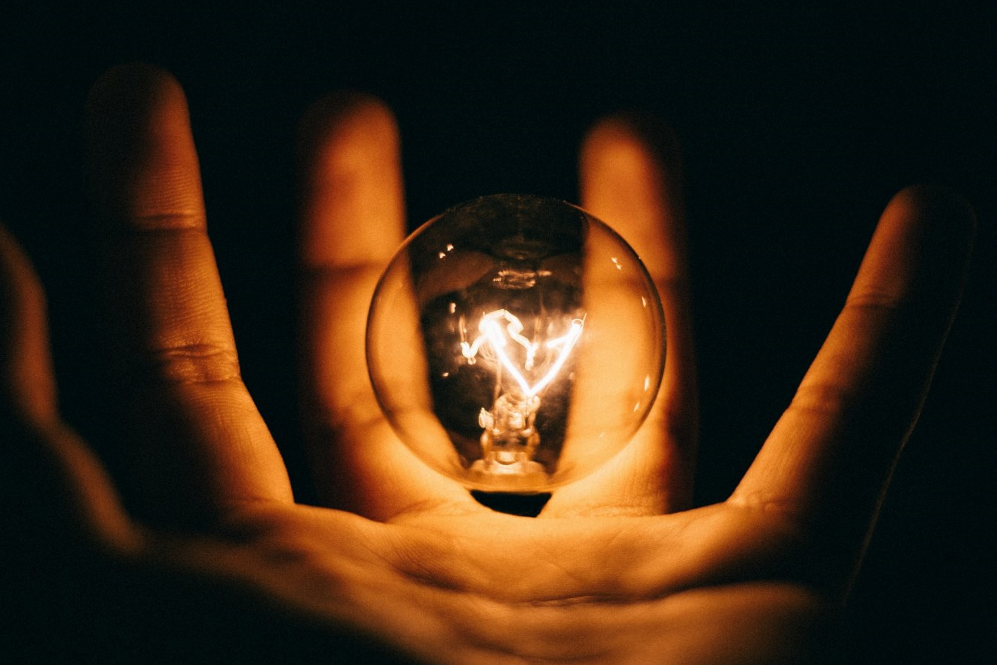 A glowing hand holding a lightbulb with a black background.