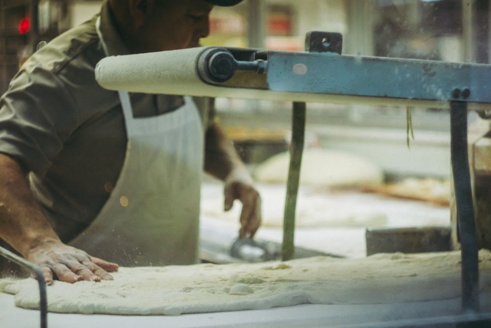 A baker rolling out dough on a bench.